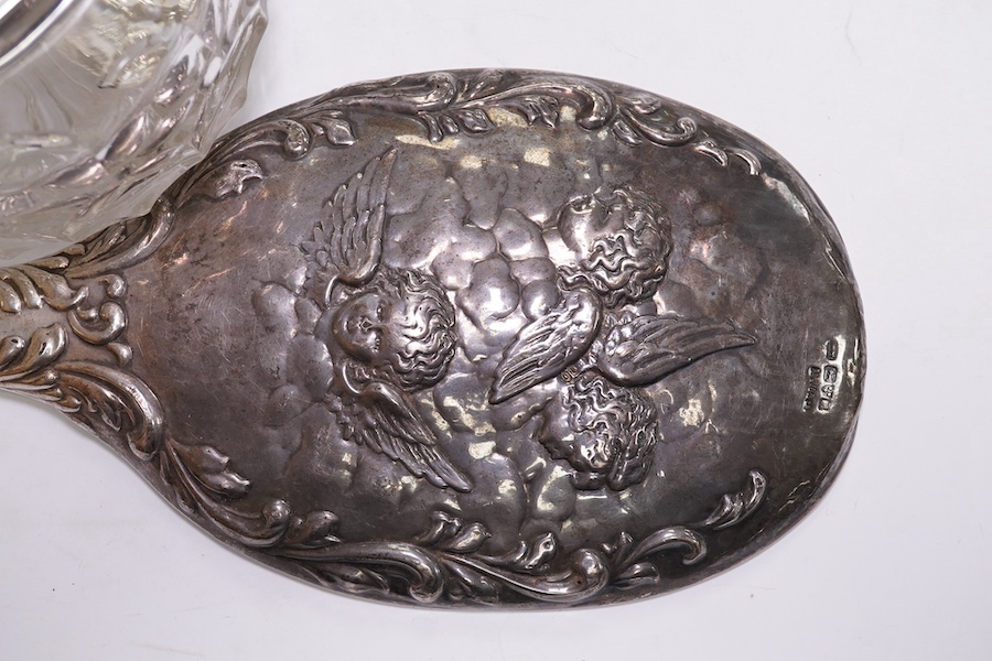 An Edwardian silver mounted hand mirror with Reynold's Angels decoration, William Neale Ltd, Chester, 1902, 26.3cm, together with a later silver mounted cut glass preserve jar and spoon. Condition - poor to fair